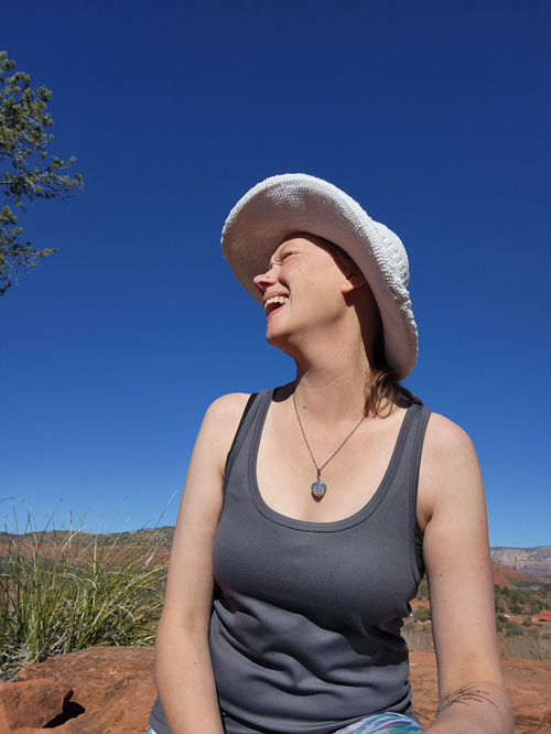 Picture of a woman facing to the left side laughing while sitting on 
   the top of a mountain